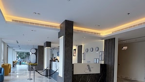 Un hall d’hôtel moderne avec un comptoir d’accueil, un sol en marbre et une vue sur la rue.