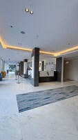 A modern hotel lobby with a reception desk, marble flooring, and a view of the street outside.
