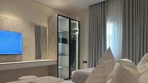 Une chambre d’hôtel moderne équipée d’un grand lit, d’une télévision, d’une armoire et d’une fenêtre avec des rideaux.