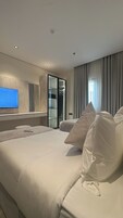 Una habitación de hotel moderna con una cama grande, televisión, armario y ventana con cortinas.