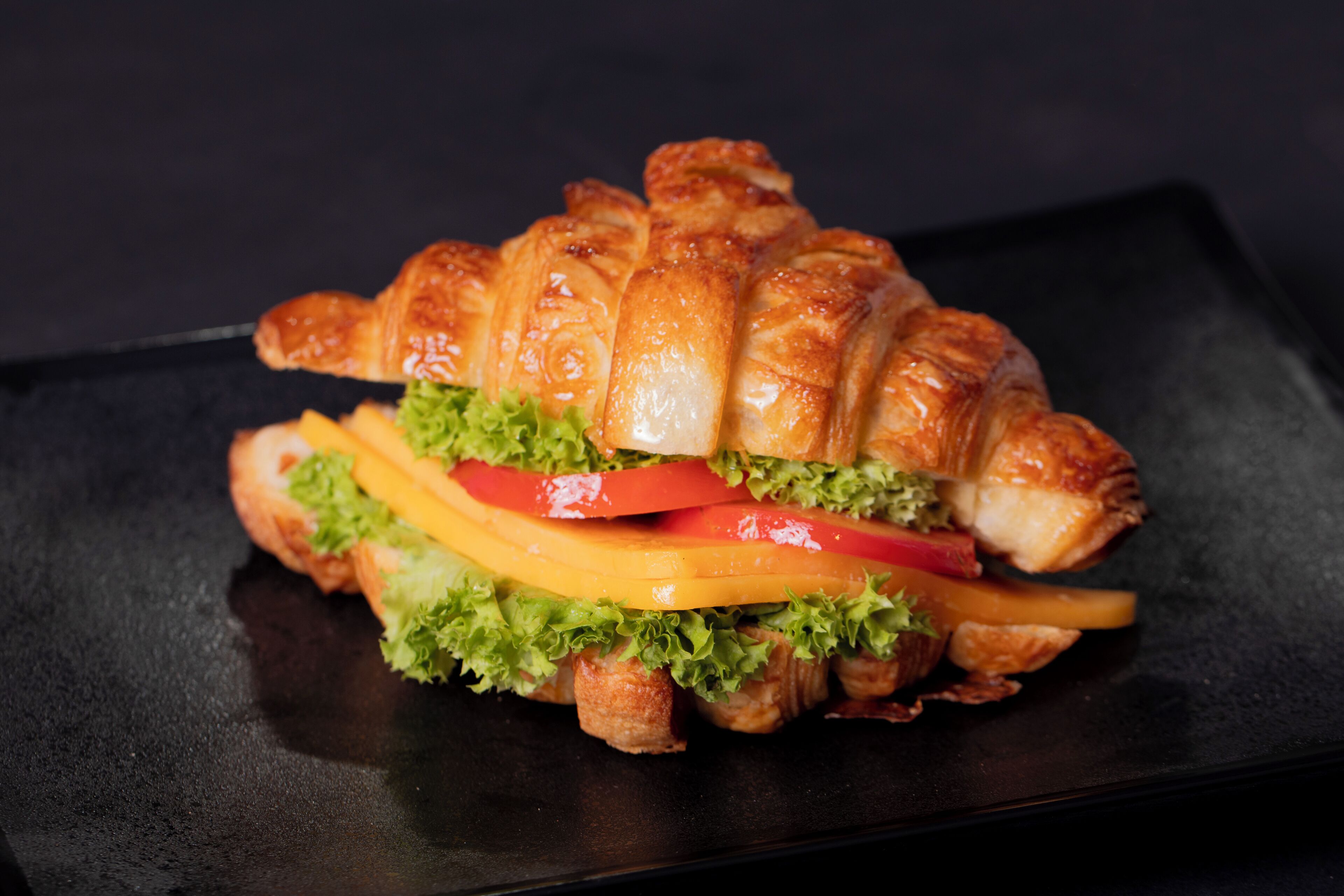 Un sándwich de croissant con lechuga, tomate y queso sobre un plato negro.