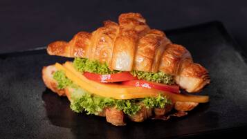 Un sándwich de croissant con lechuga, tomate y queso sobre un plato negro.