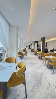 Un restaurante moderno con sillas amarillas, suelo de mármol y vistas a la ciudad.