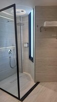 Un baño moderno con ducha de vidrio, un perchero y una ventana.