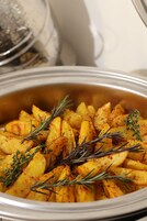 A close-up of roasted potatoes garnished with rosemary.