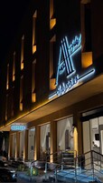 Entrada de hotel con un letrero de neón, un cartel de café y una escalera que lleva a la entrada.