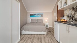 Ein kleines Hotelzimmer mit Bett, Nachttisch und einer kompakten Küchenzeile.
