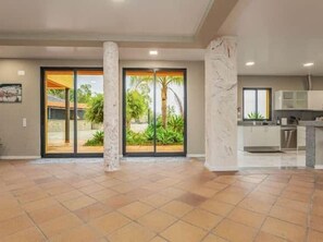 A spacious interior with a kitchen area, large sliding glass doors leading to a garden, and a tiled floor.
