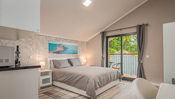 A bedroom with a bed, bedside tables, a TV, a painting, and a view of the outdoors. - Suite 3 -
Private Veranda with Ocean view (Gaula)