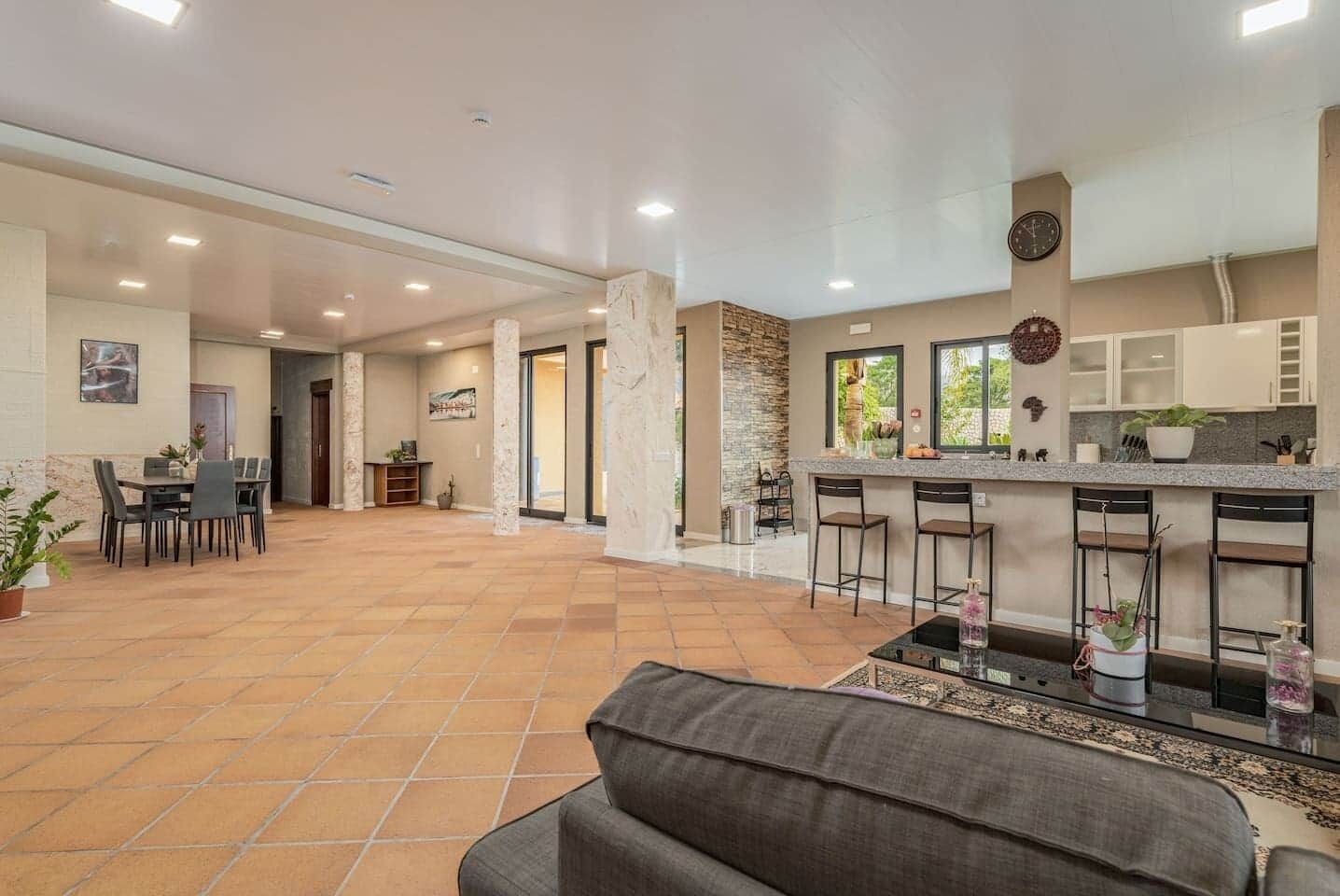 A spacious indoor area with a dining table and chairs, a kitchen with a bar, and a seating area with a sofa.
