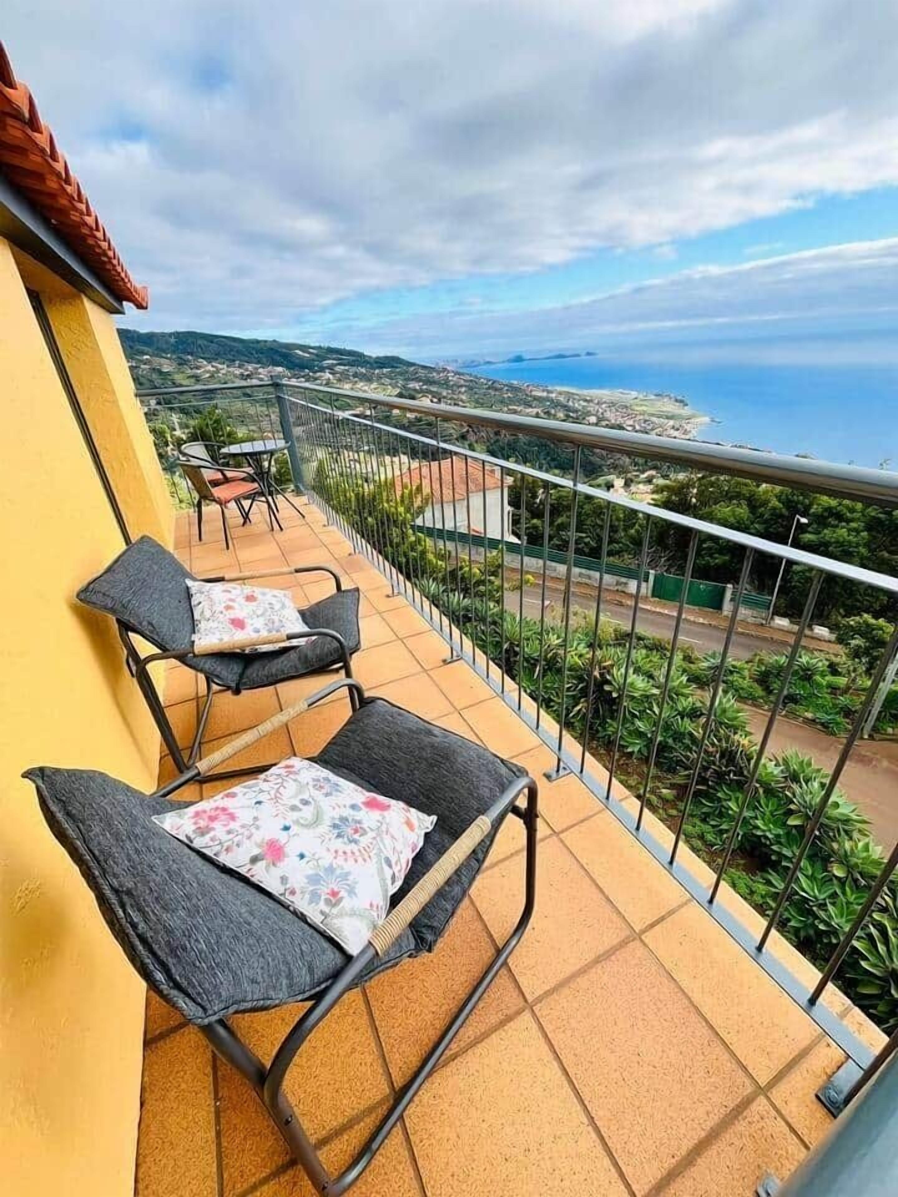 A balcony with two chairs and a table, overlooking a coastal landscape.