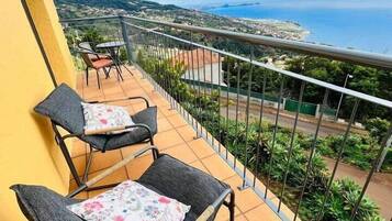A balcony with two chairs and a table, overlooking a coastal landscape.