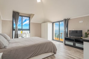 A modern hotel room with a bed, a desk, a TV, and a balcony with a view.