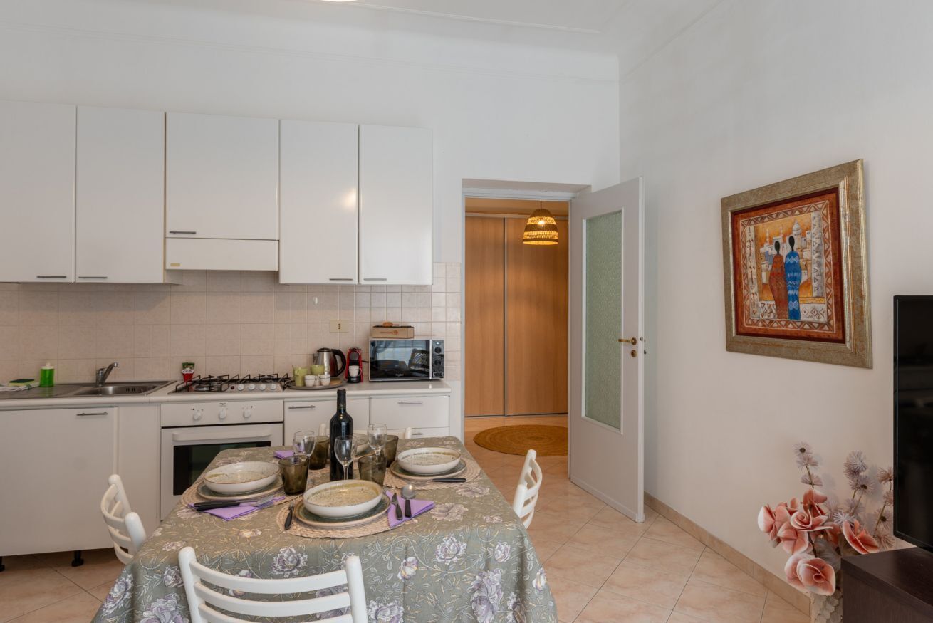 Une cuisine avec des meubles blancs, une table à manger dressée avec des assiettes et des couverts, un four à micro-ondes et une cuisinière.