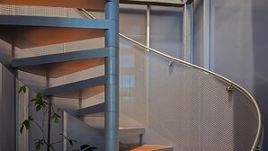 A spiral staircase with metal railings and wooden steps, a potted plant, and a window in the background. - Fishers Villa (Crescent Head)
