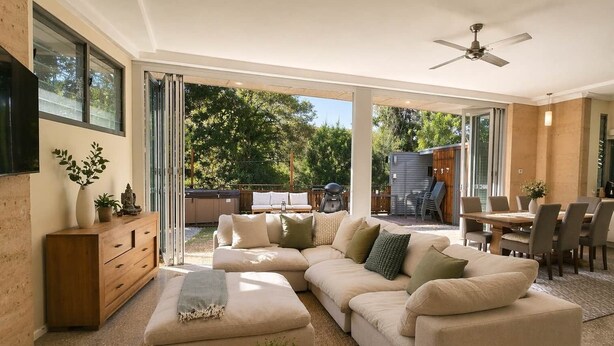 A modern living room with a sectional sofa, a wooden cabinet, and a dining area with a table and chairs. - Fishers Villa (Crescent Head)