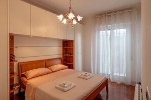 A bedroom with a wooden bed, a chandelier, a large window with sheer curtains, and built-in shelving. - GuestHost - Comfortable and spacious 58 squared meters apartment, perfect for four people, located on the sixth and top floor of a residential building with a lift (NOT suitable for disabled guests).The property is located in a central and extremely conv (Sanremo)