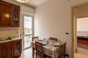A dining area with a table set for four, wooden cabinets, a kitchen counter, and a view through a glass door. - GuestHost - Comfortable and spacious 58 squared meters apartment, perfect for four people, located on the sixth and top floor of a residential building with a lift (NOT suitable for disabled guests).The property is located in a central and extremely conv (Sanremo)