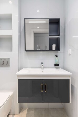 Un baño moderno con un lavamanos blanco, muebles oscuros y un espejo sobre el lavamanos.