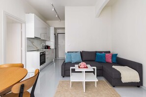 Una sala de estar moderna con un sofá gris, una mesa de centro blanca y una mesa de comedor de madera con sillas.