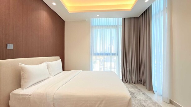A modern hotel room with a large bed, a wooden accent wall, and a view of the city through sheer curtains. - Cloud Tower 1br With Parking Pool Gym (Dubai)