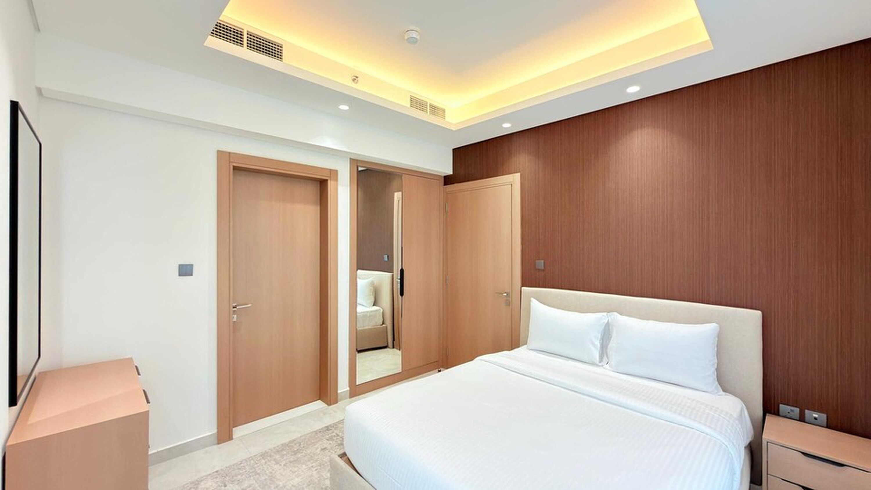 Une chambre d’hôtel moderne avec un grand lit, une armoire en bois et une petite table de chevet.