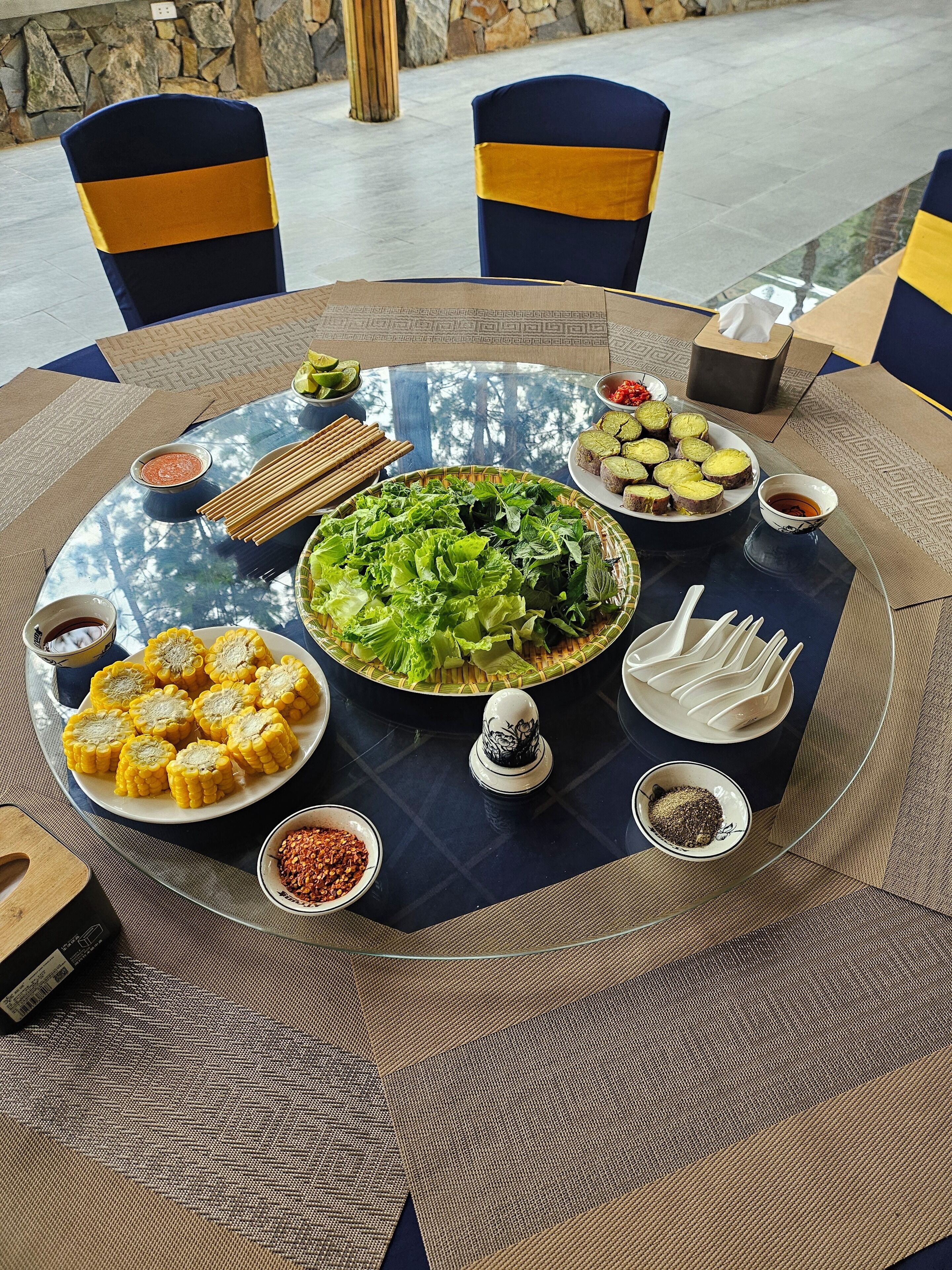 Una mesa redonda con diversos platos, como mazorca, ensalada y varios recipientes pequeños con salsas.