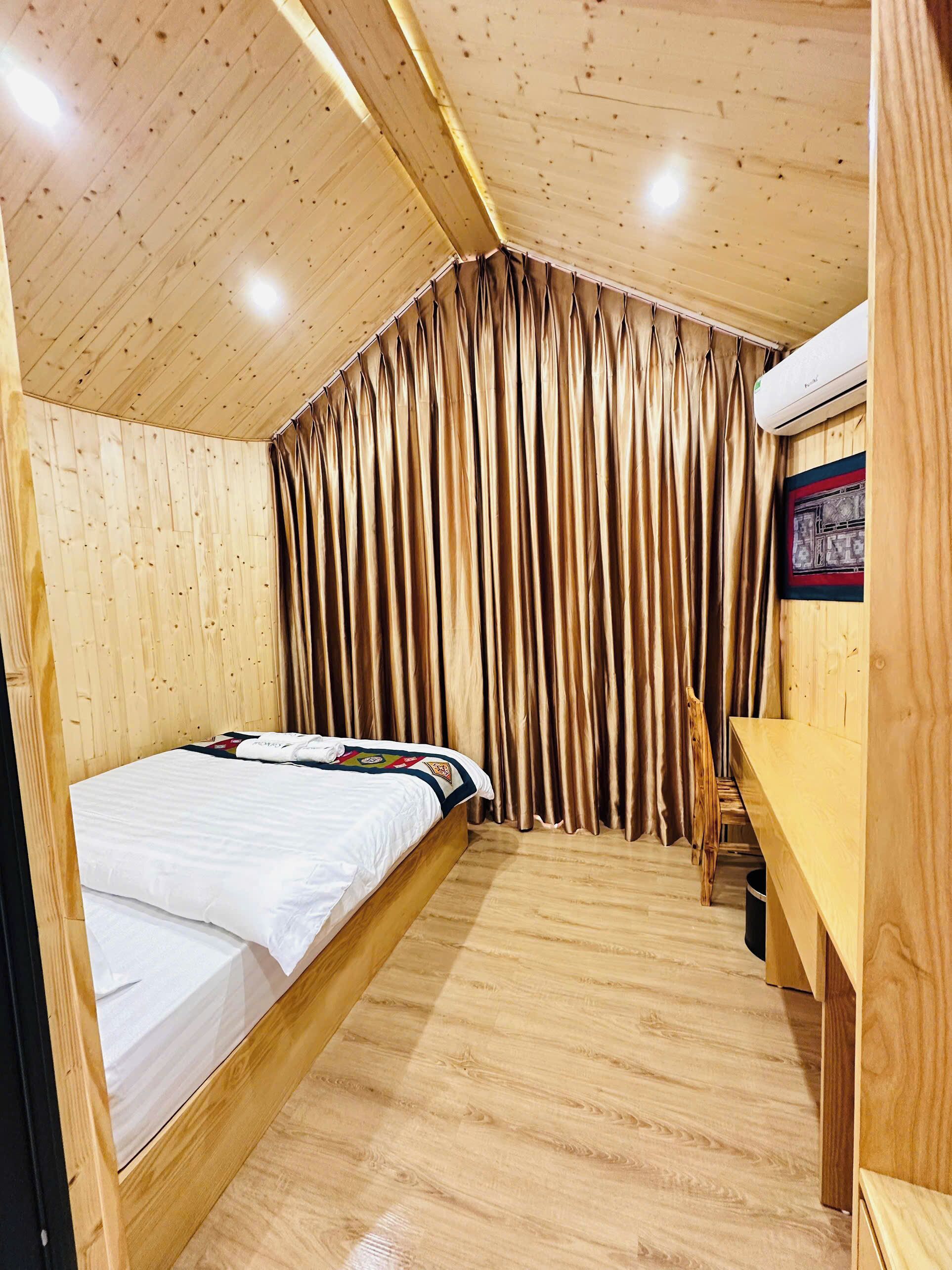 Ein Zimmer mit Holzboden, einem Bett, einem Schreibtisch und einem Vorhang.