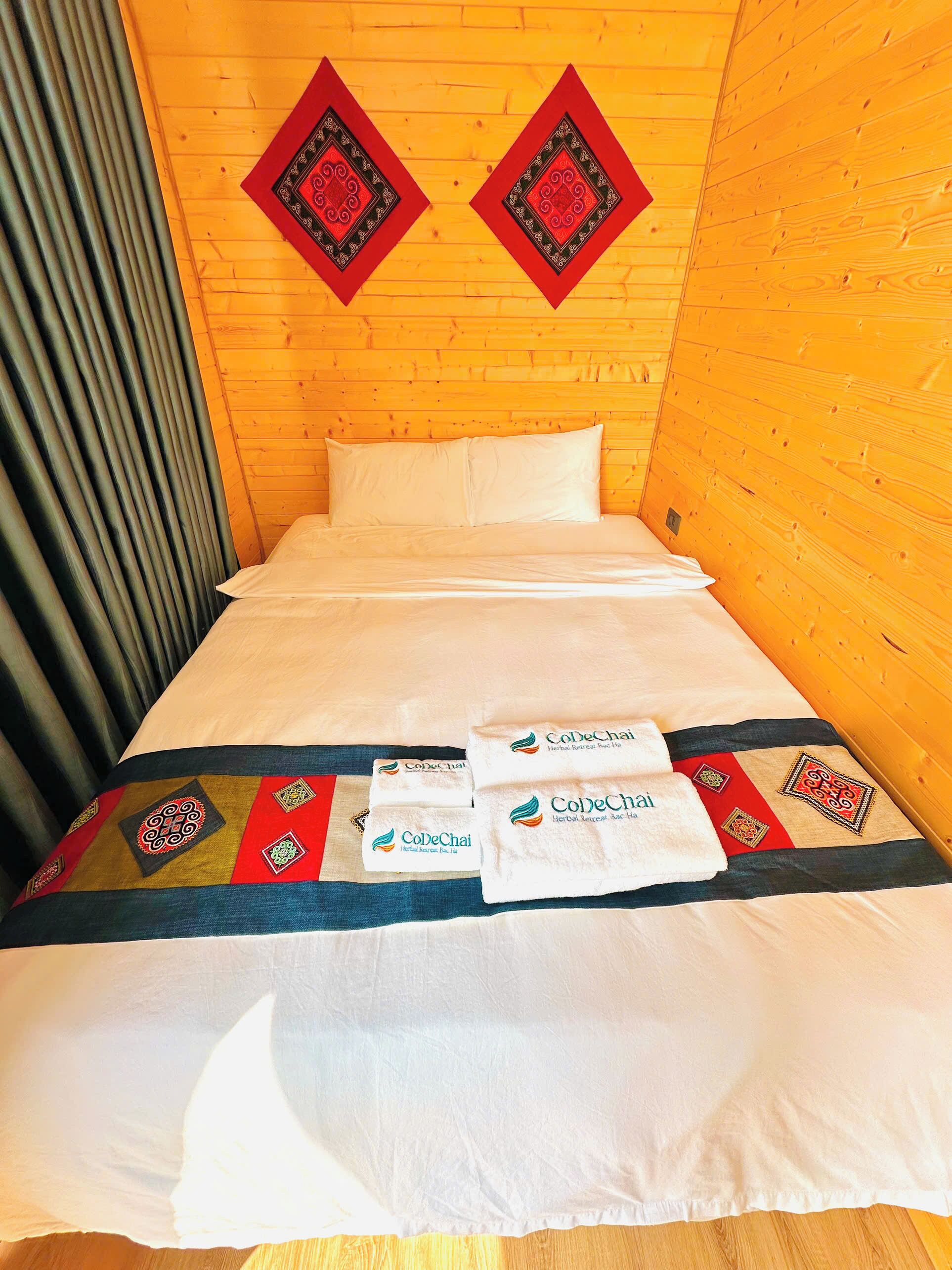 Una cama con sábanas blancas, un cabecero decorativo y dos tapices negros y rojos.