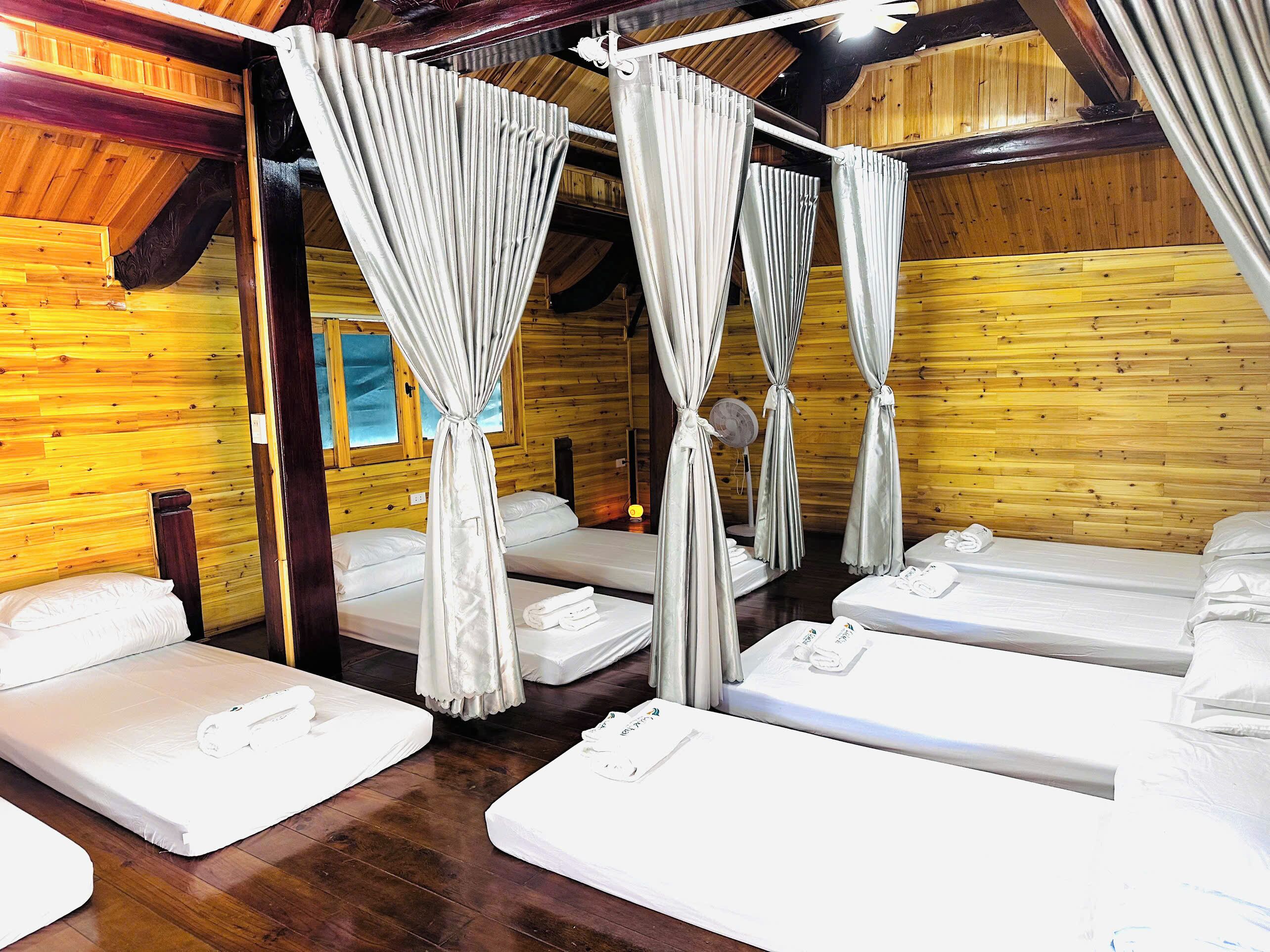 A room with four beds, each with white linens and towels, and a canopy bed with curtains.
