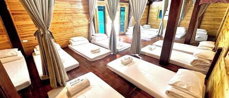 Una habitación con paredes y techo de madera, varias camas con ropa blanca y cortinas.