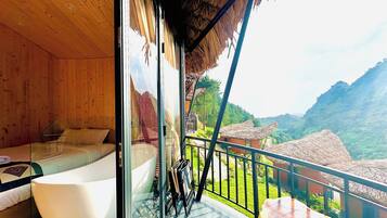 Ein Zimmer mit Glaswand, einer Badewanne und einem Balkon mit Bergblick.