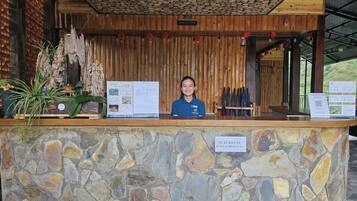 Una recepción con pared de piedra, paneles de madera y un cartel que indica 'QUÁY BÂN VÉ BE BỘI & THAM QUAN'.
