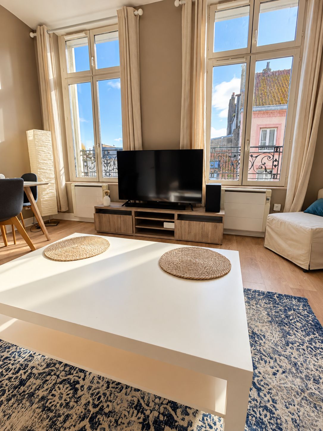 A modern living room with a flat-screen TV, a white coffee table, and a patterned rug.
