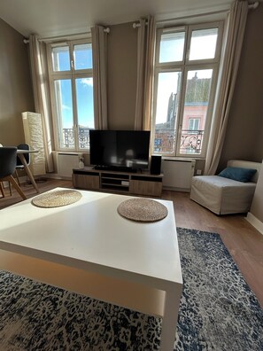 A modern living room with a flat-screen TV, a white coffee table, and a patterned rug.