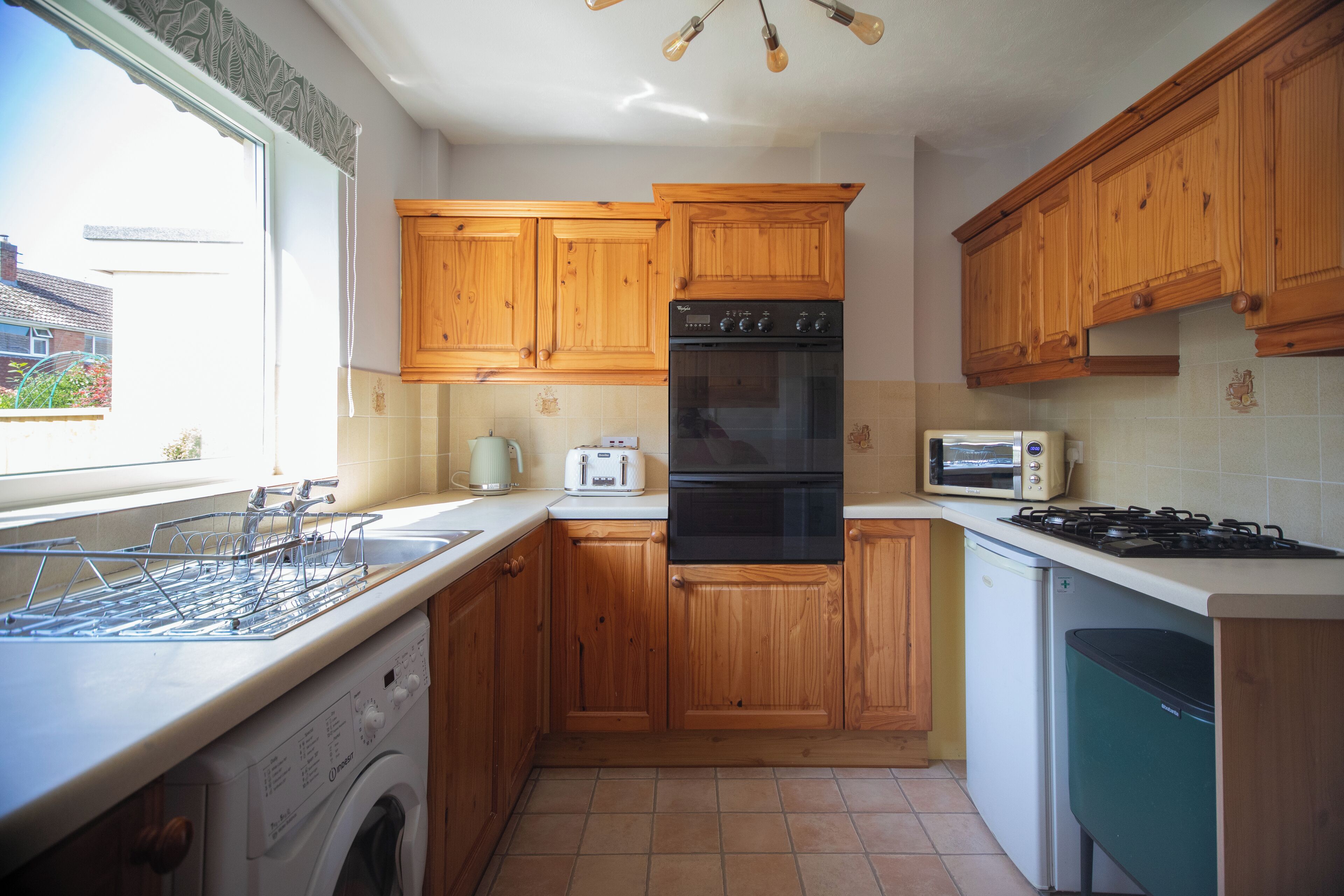 A kitchen with wooden cabinets, a washing machine, a microwave, and a gas stove.