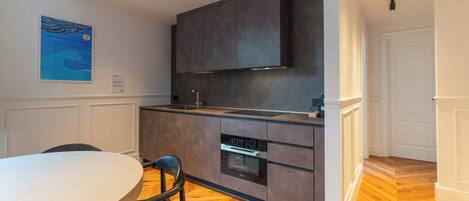A modern kitchen with dark cabinets, a built-in oven, and a dining area with a round table and chairs.