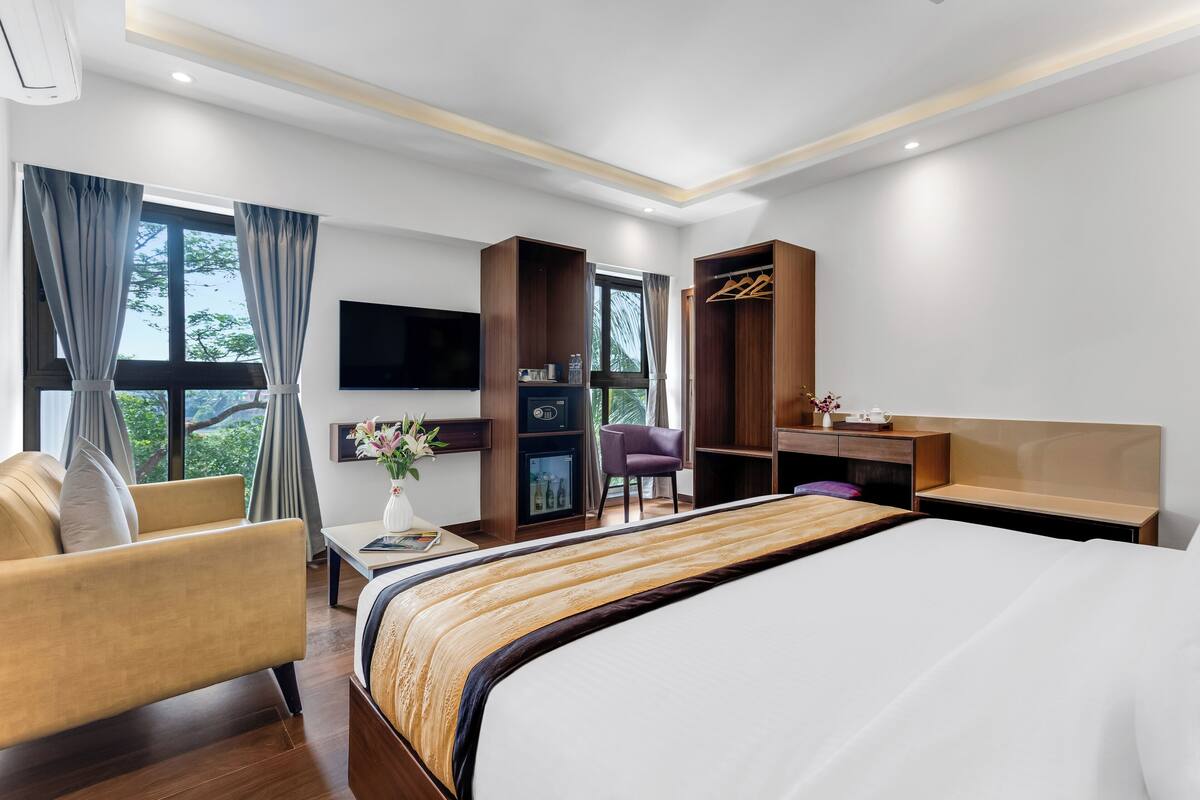 A hotel room with a large bed, a desk, a chair, a TV, and a wardrobe.