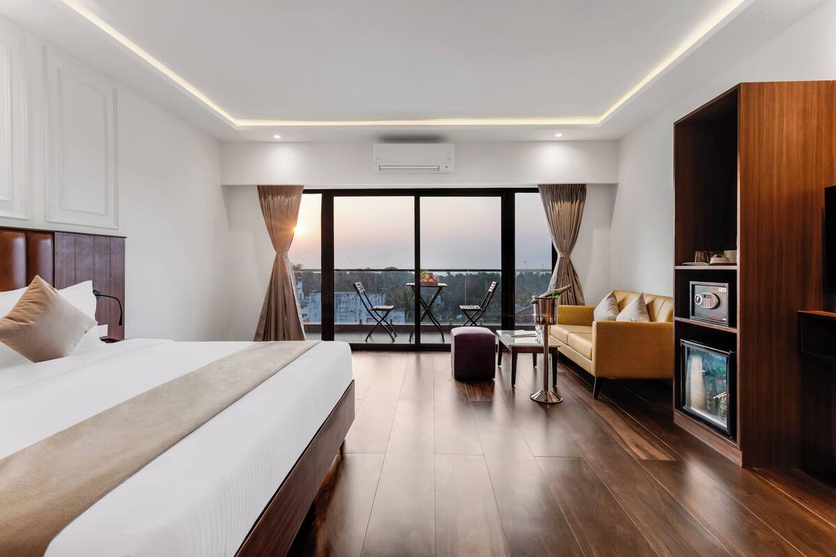 A modern hotel room with a large bed, a sofa, a TV, and a view of the cityscape.