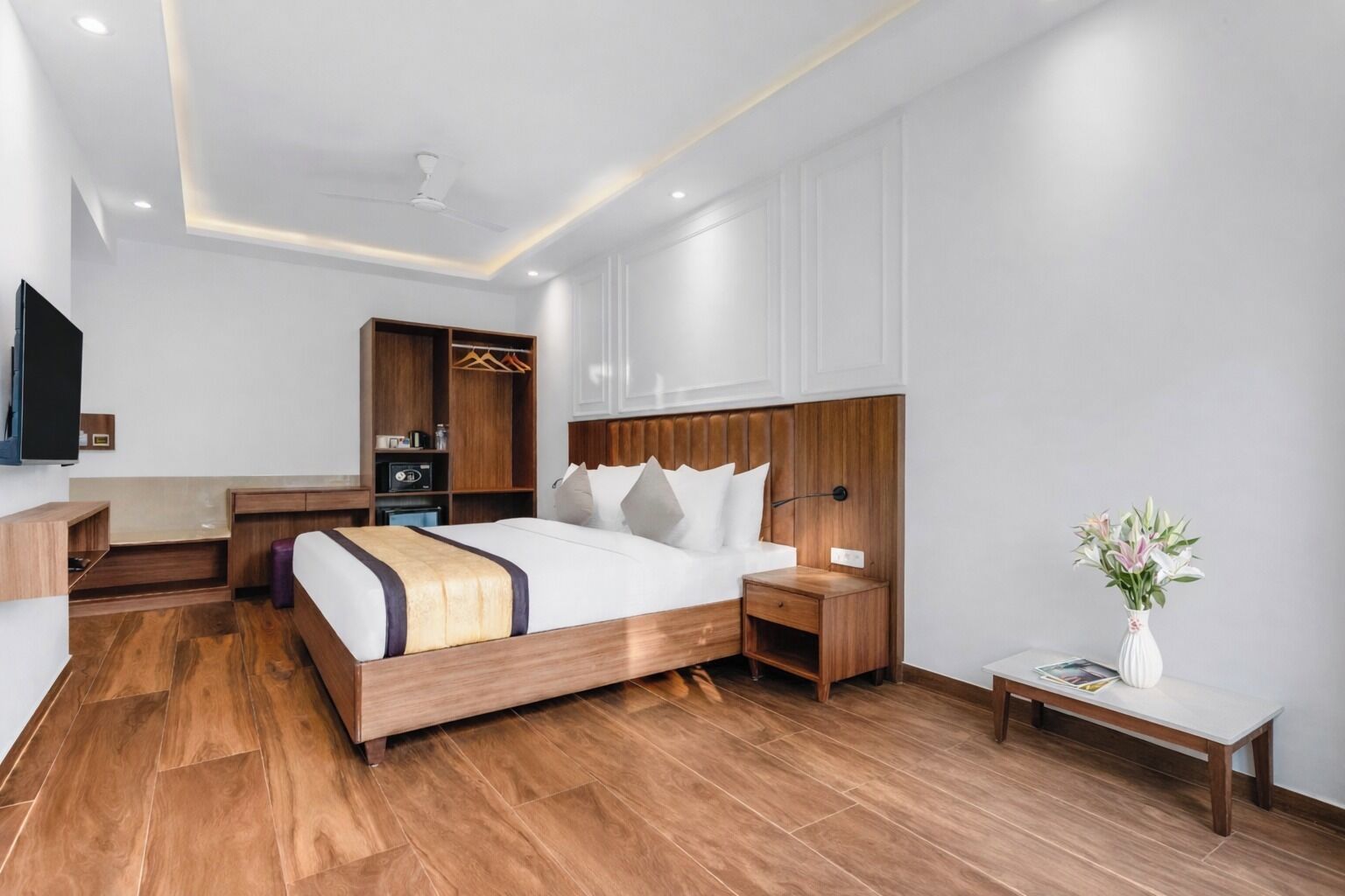 Ein modernes Hotelzimmer mit einem Holzbett, Nachttischen, einem Kleiderschrank und einem Flachbildfernseher.