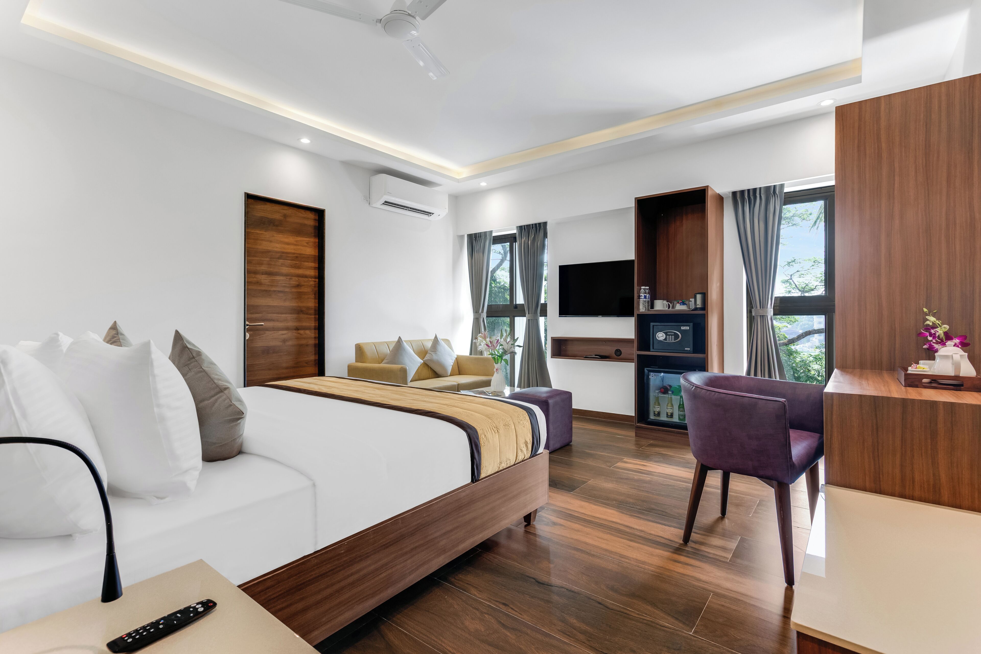 Habitació d'hotel moderna amb un llit de fusta, un sofà, un escriptori i una televisió.
