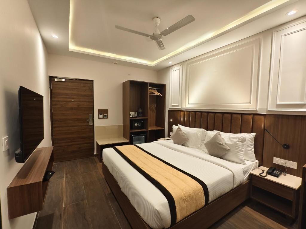 A modern hotel room with a bed, wardrobe, TV, and built-in shelves.