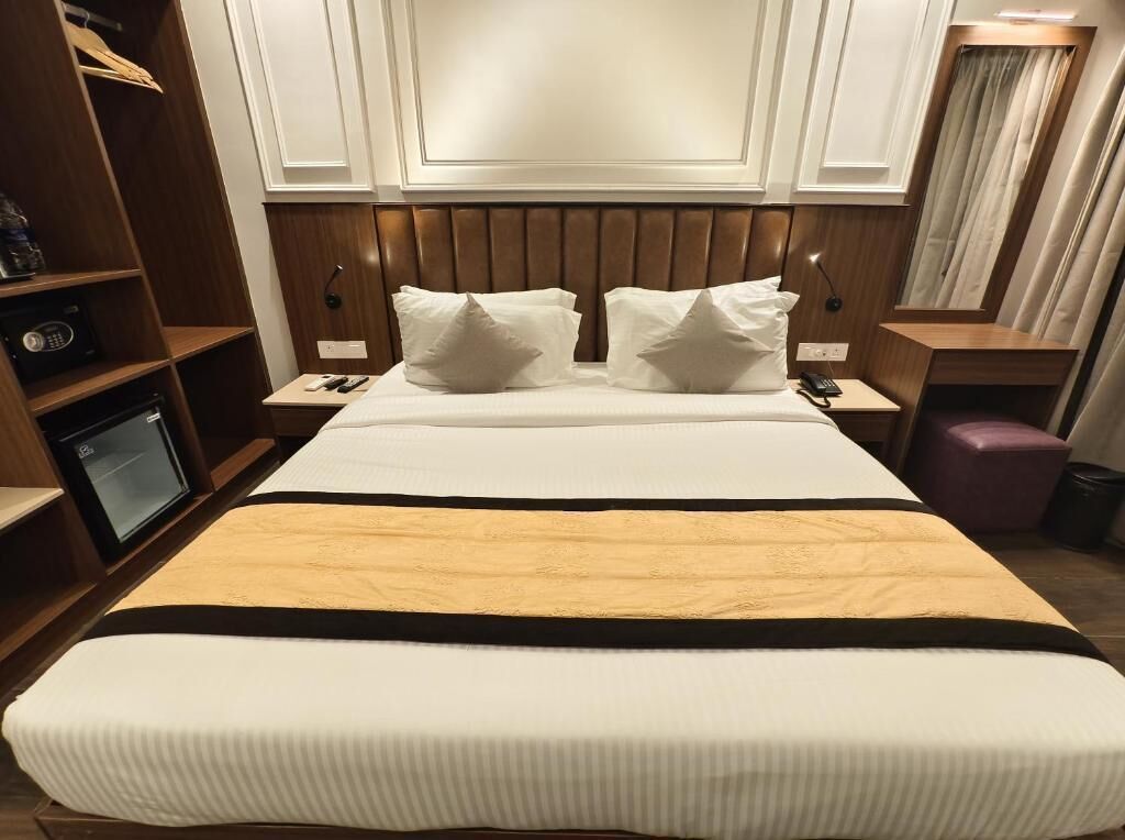 A hotel room with a large bed, wooden headboard, bedside tables, a wardrobe, and a small desk with a lamp.