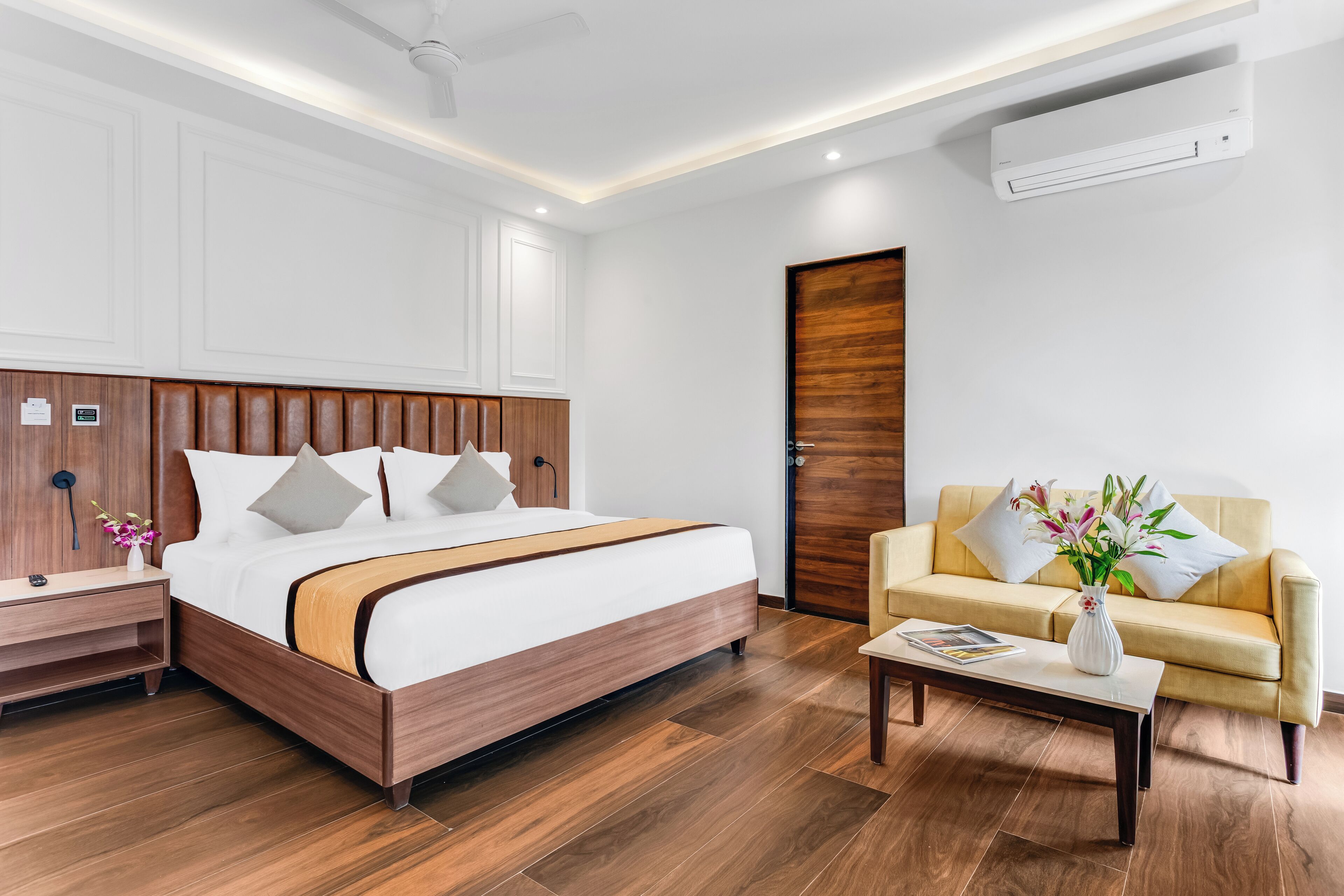 Una habitación de hotel moderna con una cama de madera, un sofá, una mesa de centro y un jarrón con flores.