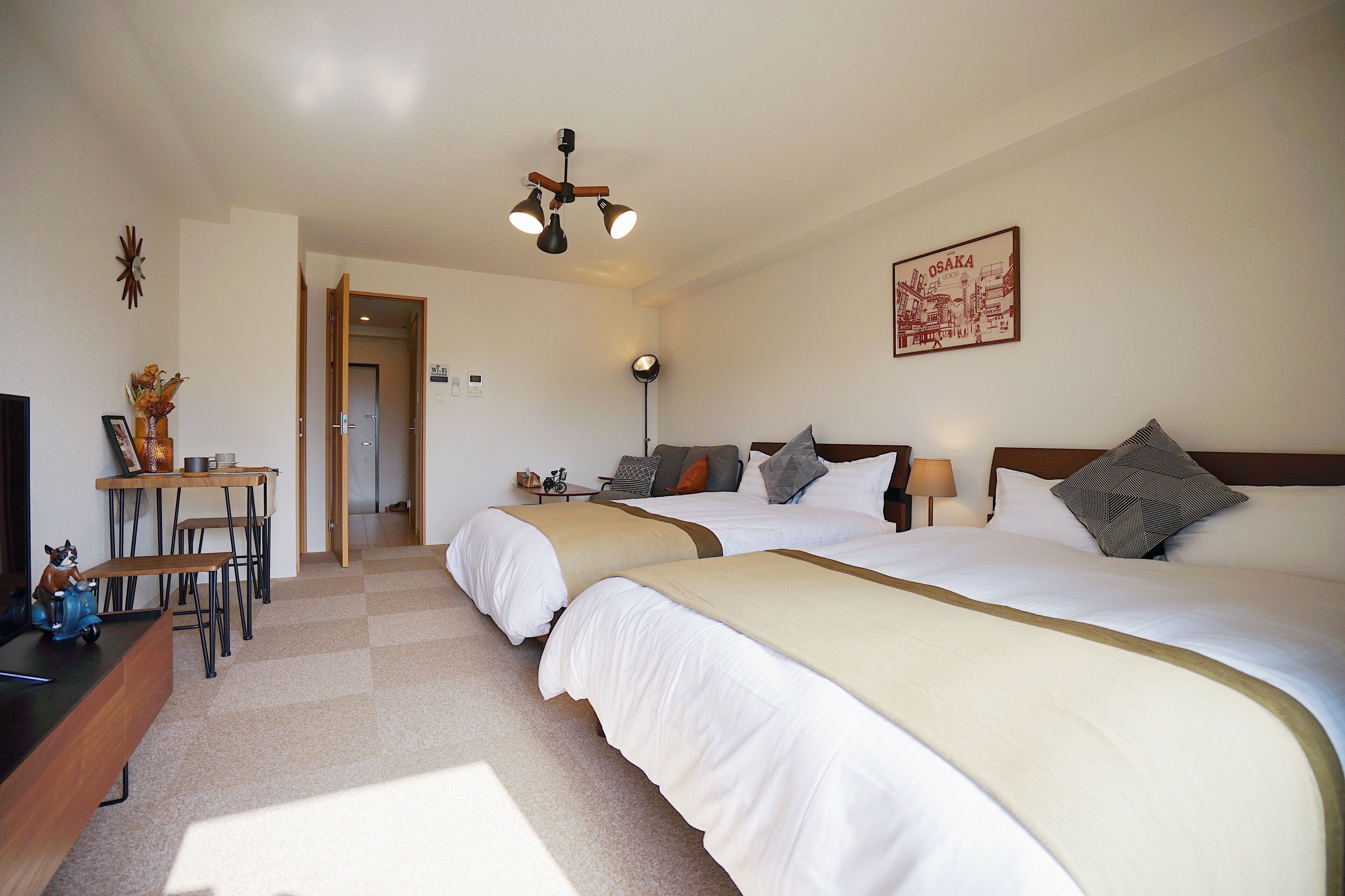 A hotel room with two beds, a desk, a chair, a TV, and a ceiling fan.