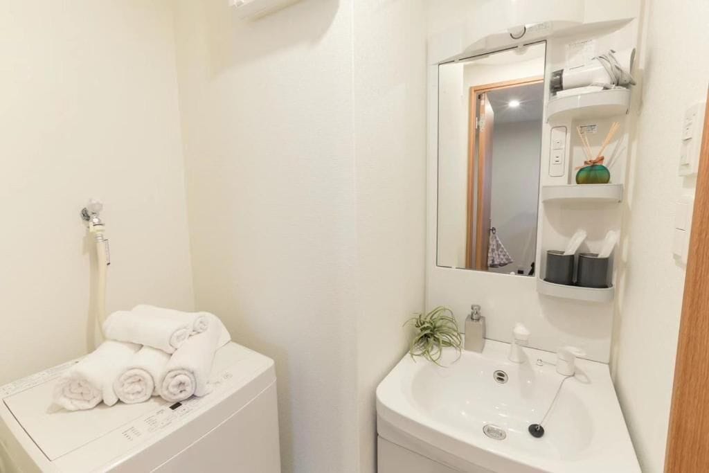 A bathroom with a toilet, a sink, and a mirror. There are towels on the toilet and a small plant on the sink.