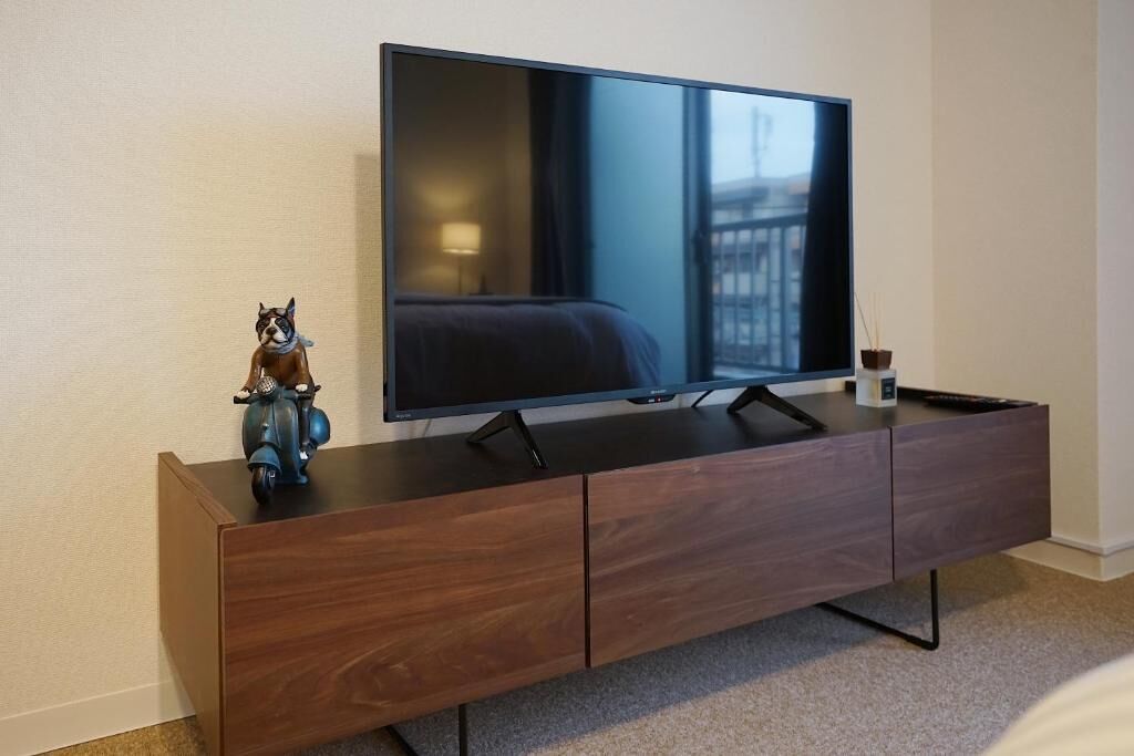 A modern hotel room with a large flat-screen TV on a wooden console, a small figurine, and a potted plant.