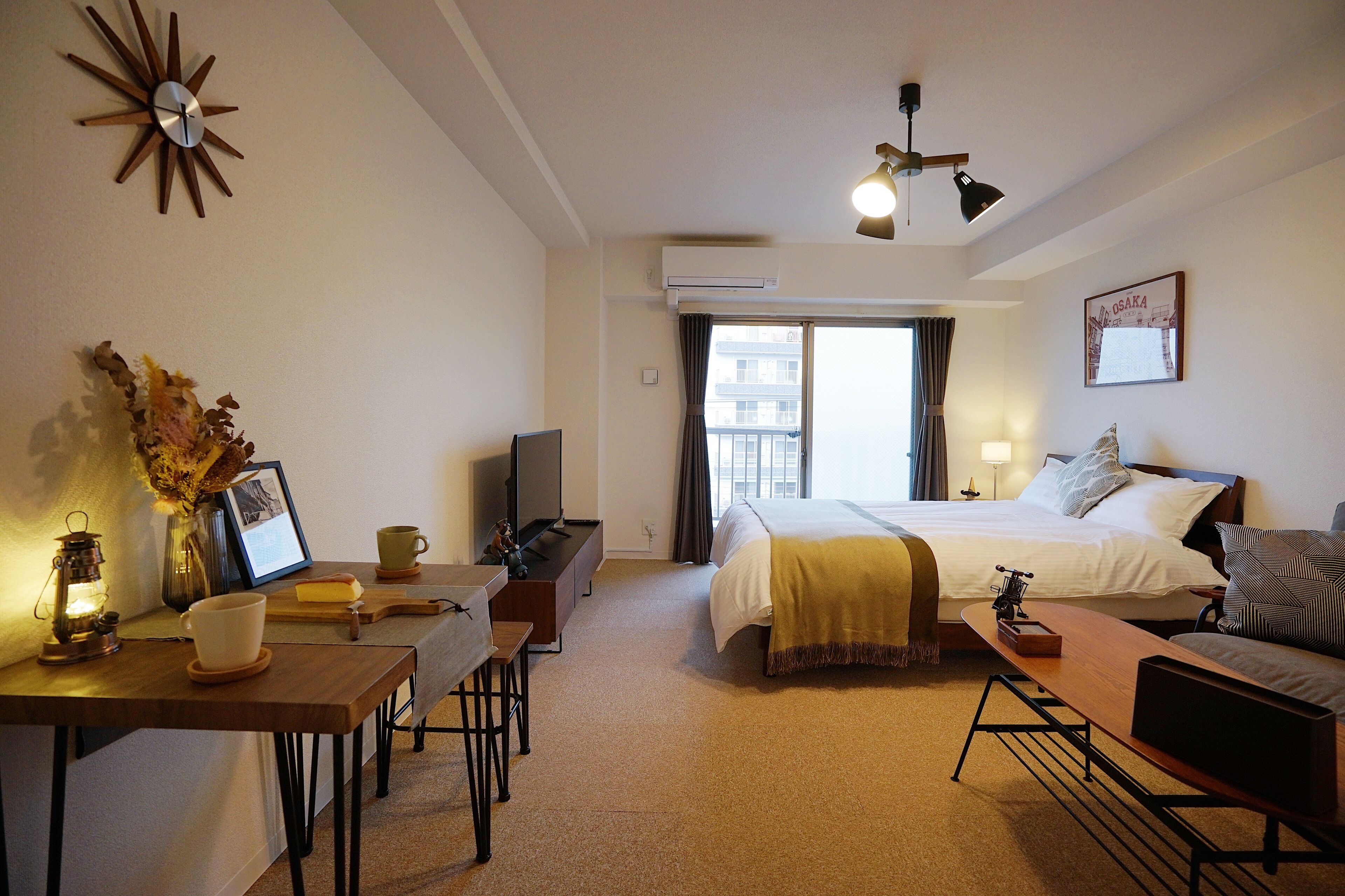A hotel room with a bed, a desk with a lamp, a TV, and a window with curtains.