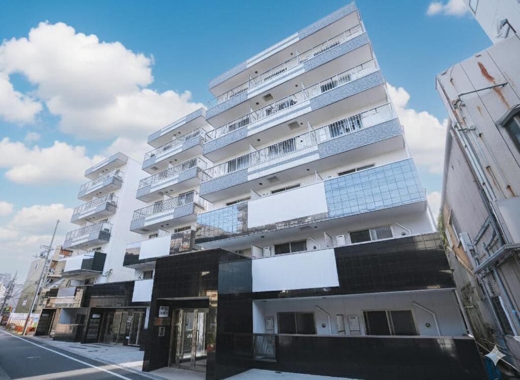 A multi-story residential building with balconies, a ground-level entrance, and a clear sky.