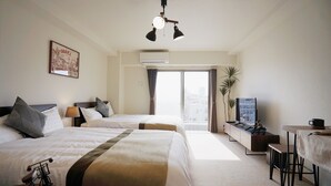 Habitació d'hotel amb dos llits, una taula de treball, un televisor i una finestra gran.